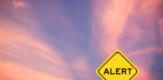 Yellow alert sign against a colorful sunset sky