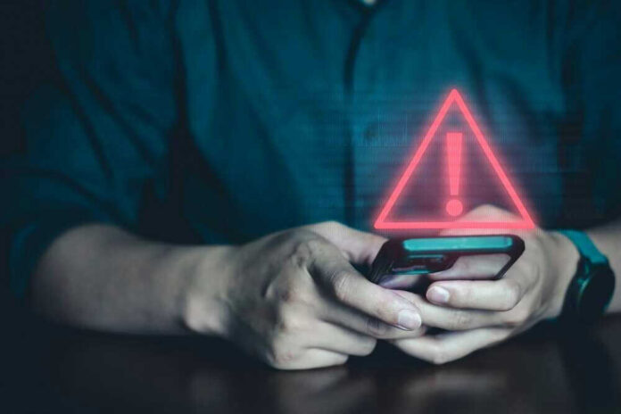 shutterstock_2342619545.jpg Person holding phone with warning symbol displayed.