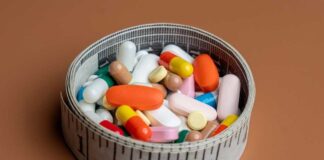 A bowl filled with various colorful pills and capsules next to a measuring tape