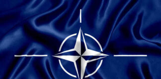 NATO flag with white compass emblem on blue background.