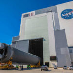 Massive rocket component outside NASA assembly building under clear sky.