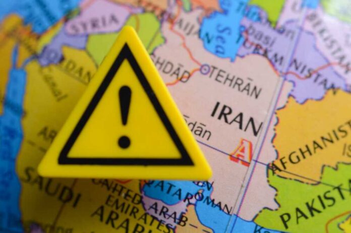 shutterstock_2732699345.jpg A yellow warning sign placed on a map highlighting Iran