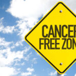 A yellow warning sign that reads 'CANCER FREE ZONE' against a blue sky