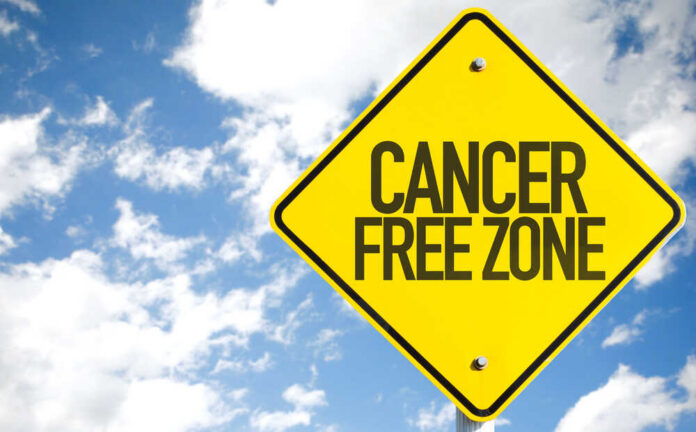 A yellow warning sign that reads 'CANCER FREE ZONE' against a blue sky