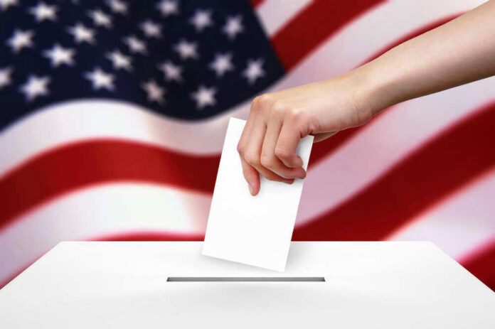 Hand dropping ballot into box, American flag background.