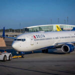 Delta airplane being towed at airport terminal gate.