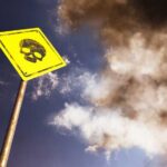 A yellow warning sign with a skull symbol against a cloudy sky