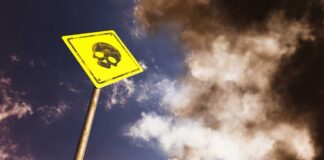 A yellow warning sign with a skull symbol against a cloudy sky