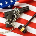 A handgun chained on an American flag with a gavel beside it