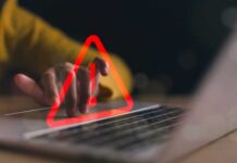 A hand hovering over a laptop keyboard with a warning symbol displayed