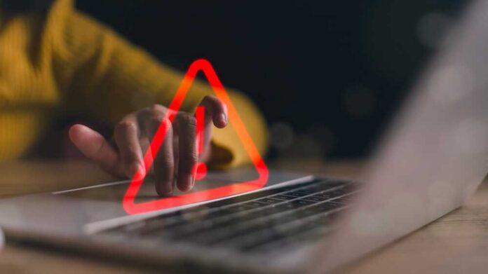 A hand hovering over a laptop keyboard with a warning symbol displayed