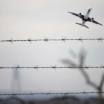 Airplane taking off view through barbed wire fence