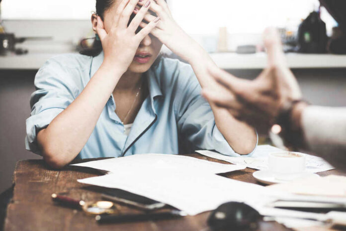 shutterstock_481953475 Stressed woman with hands on face at a desk.